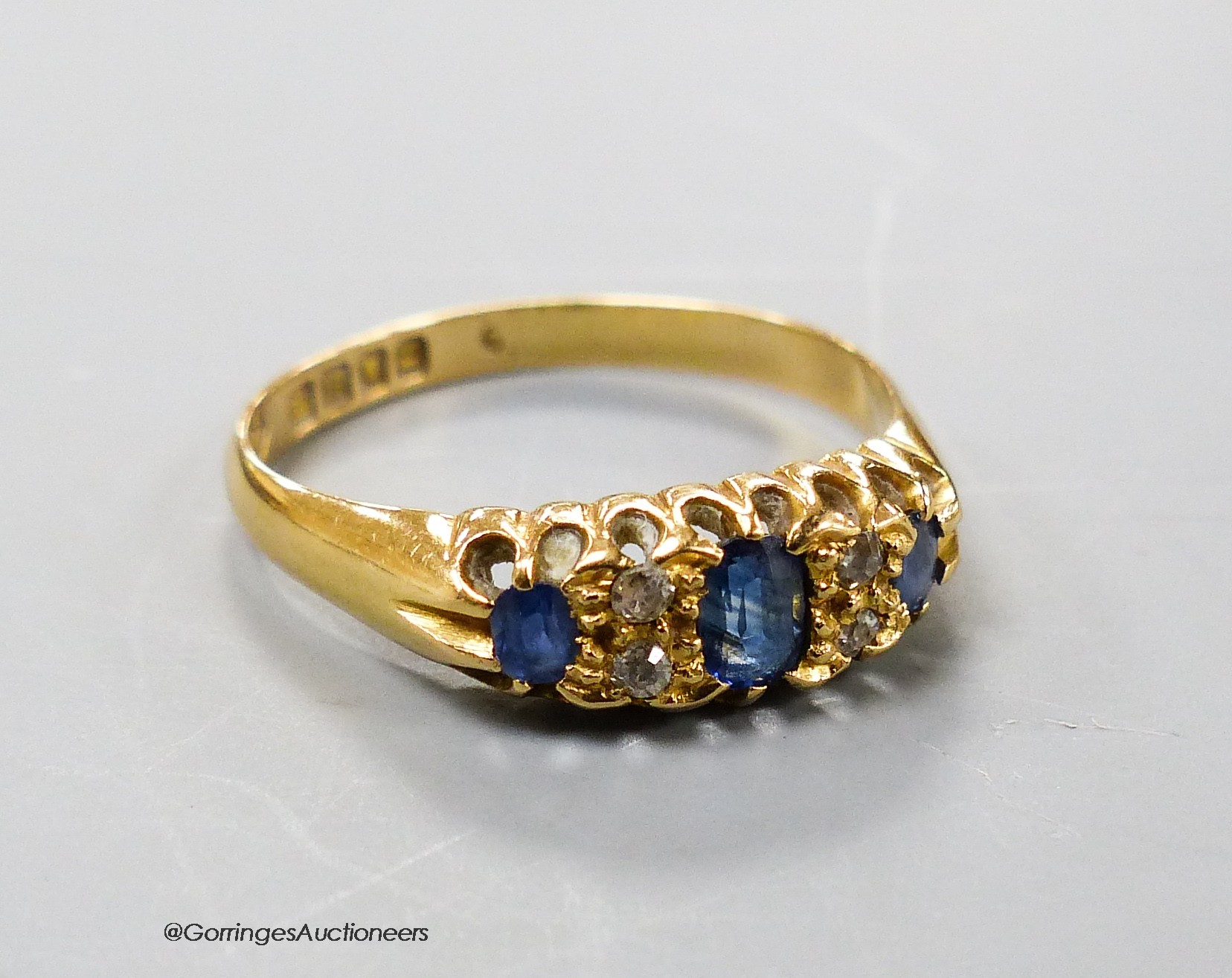 An Edwardian 18ct gold, three stone sapphire and diamond chip set ring, size R, gross weight 3.1 grams.